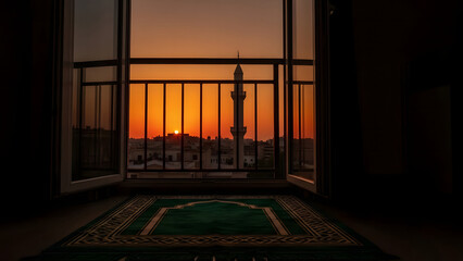 Obraz premium Sunset view from a window with a prayer mat and a cityscape featuring a mosque tower in the distance
