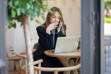 Relaxed businesswoman working on remote in cafe, using laptop and talking on smartphone with...