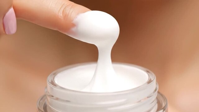 Finger dips into white cream in clear jar
