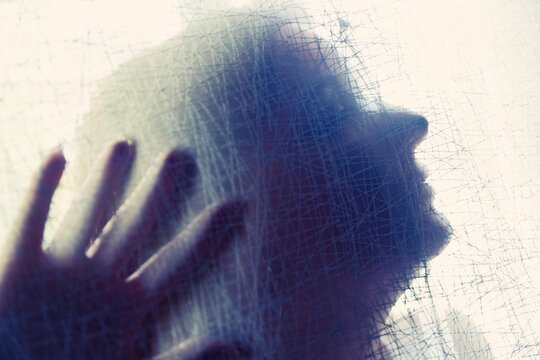 Silueta tras superficie transl&uacute;cida texturizada con mano extendida.aislamiento y presencia, simbolizando tensi&oacute;n emocional, identidad y abstracci&oacute;n humana.