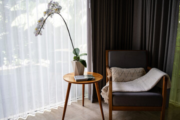 Bright room in soft white tones with a relaxing chair and a table decorated with a white orchid, creating a calm and elegant atmosphere.