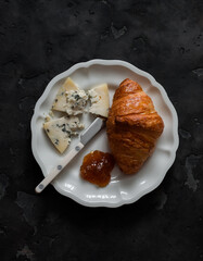 Croissant, fig jam and gorgonzola cheese on a dark background, top view. Delicious breakfast, snack, dessert