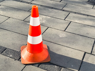 Orange traffic cone on urban sidewalk casting shadow.