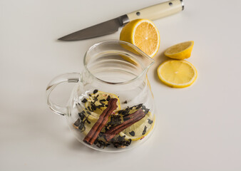 Making green tea with cinnamon stick and lemon in a glass teapot on a light background