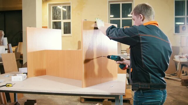 Carpenter working with an electric screwdriver on the factory, fixing wooden furniture details