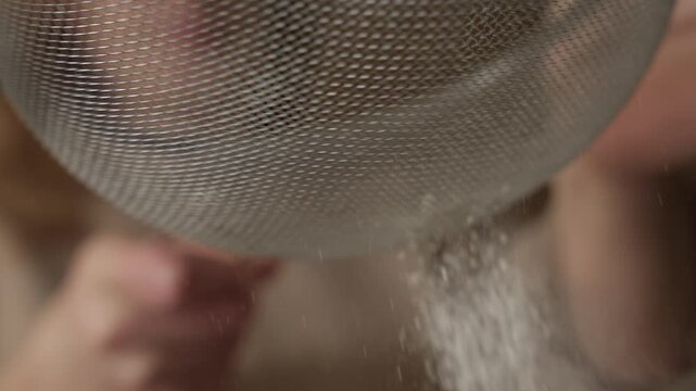 Slow motion close up of fine powder falling through kitchen sieve