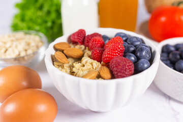Healthy balanced breakfast with oatmeal, fresh berries, almonds, milk, juice and vegetables on...