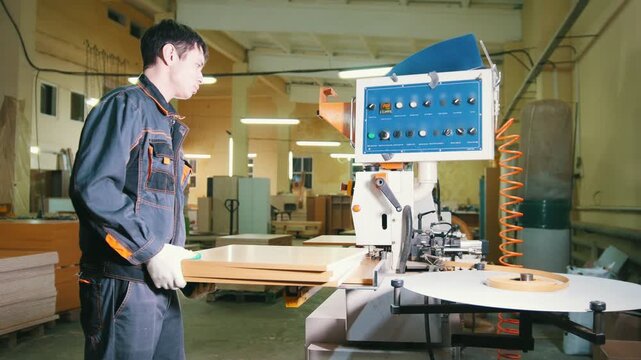 Worker carpenter handles wooden panels on the edging machine on the furniture factory