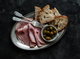 Delicious appetizer, tapas, snack - ham, sourdough bread, olives on a metal plate on a dark background