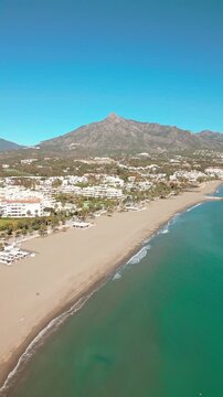 Vertical aerial view of Marbella beach, Costa del Sol, Southern Spain, with iconic La Concha mountain in the background on a bright Mediterranean day.