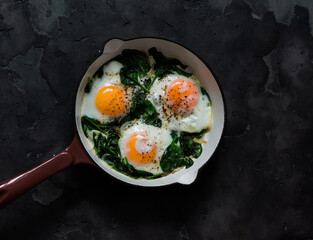 Fried eggs with spinach in a cast-iron skillet on a dark background, top view