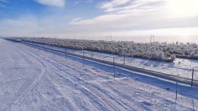 A train is traveling on a winter railway, and the trees are covered in white frost.