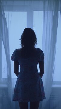 unrecognizable black dark silhouette Unhappy woman standing looking at window, mood depression sadness loneliness emotion. Mystery Girl back rear view. wind blows curtains fly waving white fabric. 4k