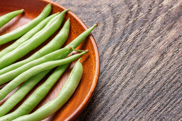 Closeup view of fresh green beans on wooden plate