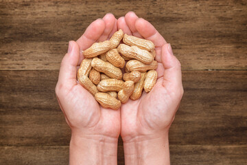 Opened female palms with fresh peanuts on wooden background