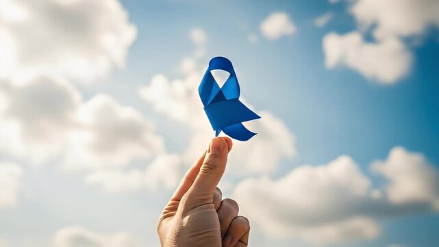 Hand holding blue ribbon against cloudy sky symbolizing hope and awareness.