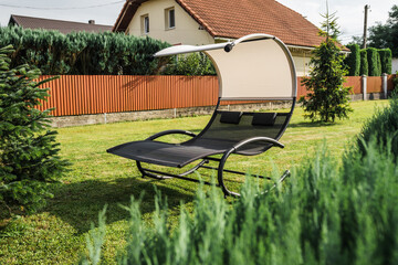 Garden swing chair on a short green lawn in the backyard on a bright sunny day.