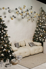 Decor in a photo studio on a New Year and Christmas theme, decorated Christmas trees with toys, garlands and white furniture on a white wall background and balls hanging from the ceiling