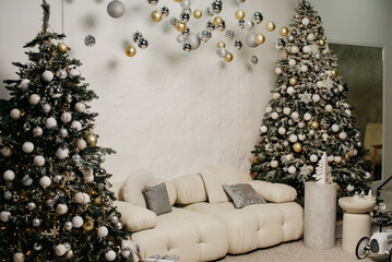 Decor in a photo studio on a New Year and Christmas theme, decorated Christmas trees with toys, garlands and white furniture on a white wall background