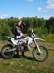 Obraz premium Woman rider of an off road motorcycle posing with her helmet on a dirt track. Extreme sport and adventure concept. Outdoor activity.