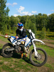 Woman in protective gear sitting on motocross motorcycle at an outdoor track. Adrenaline sport and extreme riding in nature for active lifestyle.
