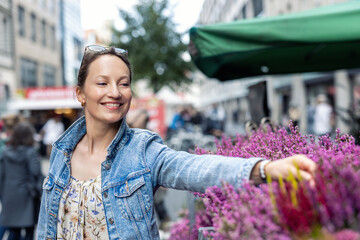 Young adult joyful woman choose to buy colorful potted flowers at outdoor market stall. Female...