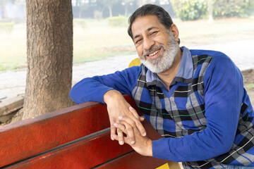 Fototapeta premium Indian happy senior man feels freedom, fun and spending leisure time while looking at the camera at the park after retirement