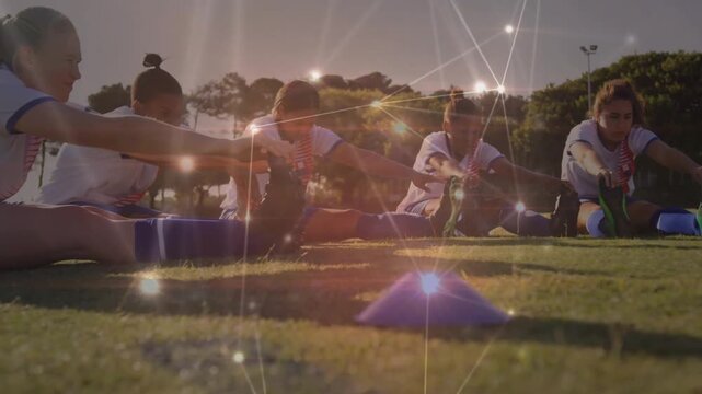 Four soccer teammates performing hamstring stretch after whistle on field with cones and ball