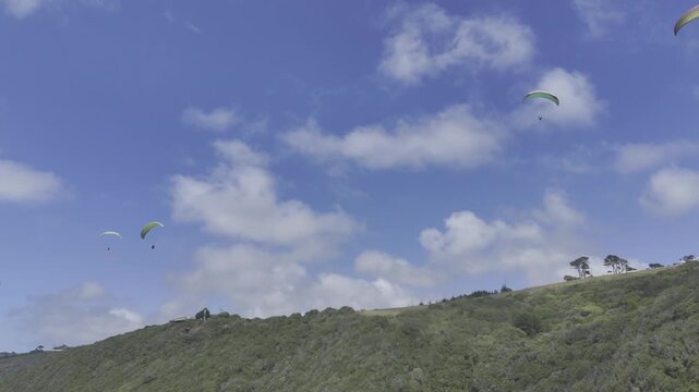 Drone flies backwards below paragliders as camera pans down to reveal coastal highway on a sunny day on the Garden Route in Wilderness, South Africa