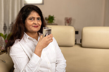 Indian matured woman drinking clear water at home. Mature  lady staying hydrated after sports.  Healthy lifestyle and wellness concept