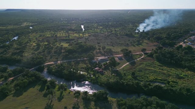 High-altitude drone reveals Cerrado hydrology complexity: multiple blue-water perennial river systems meandering through savanna mosaic, visible smoke plume indicating fire management