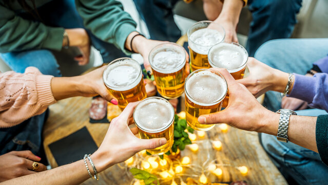 Group of people drinking beer at brewery pub restaurant - Happy friends enjoying happy hour sitting at bar table - Closeup image of brew glasses - Food and beverage lifestyle concept