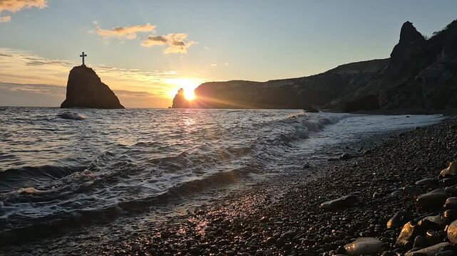 Sunset, sea, waves. Sunset sea waves crash onto a pebble beach beneath dramatic cliffs and rocky islands. Vertical video