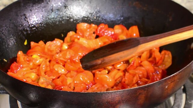 close-up shot of a vibrant mix of chopped red and orange sweet chili peppers being fried in a dark metal pot, essential first step of a homemade stew or "sofrito"