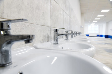 Several new and clean sinks with the same shiny chrome faucets are lined up in a row.