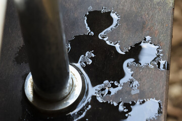 Industrial spilled liquid oil leak stain on rusty steel surface creating abstract pattern with wet dark reflection conveying messy damaged emotion from broken machine