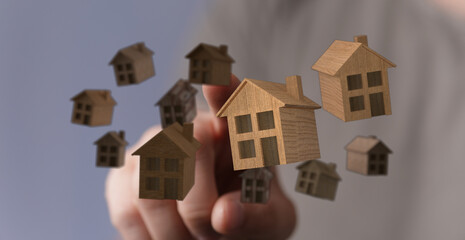 Close-up of hand interacting with multiple wooden houses, representing concepts of home, property, and real estate. Symbolizes investment and se