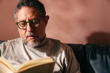 Middle aged man reading a book at home, calm and focused moment
