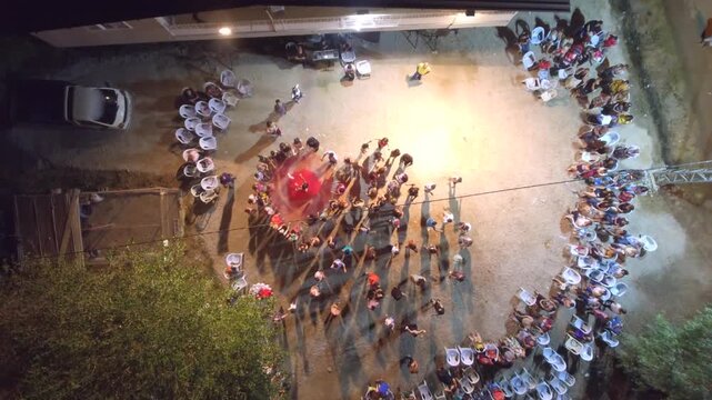 Kurdish halay dance circle showing red dressed Kurdish woman performing joyful ethnic celebration. Traditional folklore gathering captured from aerial drone view using festive rhythm.