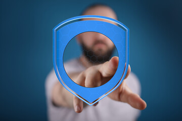 A man's finger touches a digital shield icon representing security, protection, and data privacy. Blue background. Concept of safety