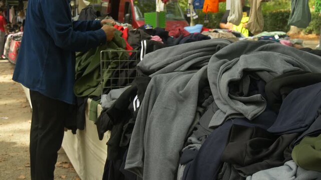 Male Shopper Looking through Pile of Used Clothes at Street Market Promoting Conscious Consumption and Eco Lifestyle