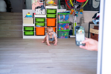 Parent taking photo of baby crawling on the floor at home