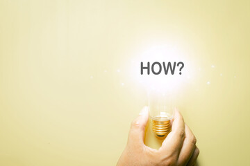 Hand holding light bulb with How word. Concept of finding answers, problem solving, asking questions, and brainstorming ideas on yellow background with copyspace or freespace.