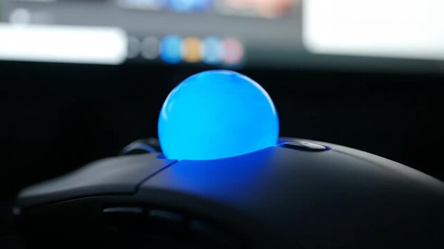Ergonomic trackball mouse with blue illuminated ball near monitor, technology concept.