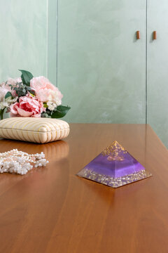 Still life of a orgonite pyramid on a table with a bouquet of pink flowers on a green background
