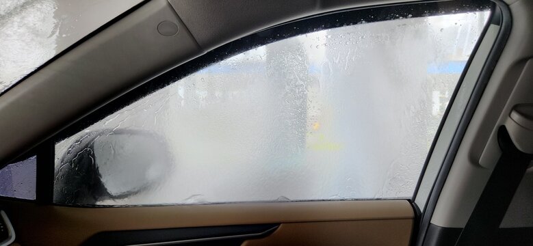 Fogged side window with water streams inside automatic car wash, interior view