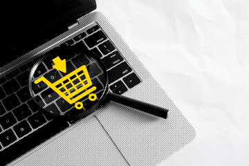 Magnifying glass on laptop keyboard with yellow shopping cart symbol. Online shopping search,...