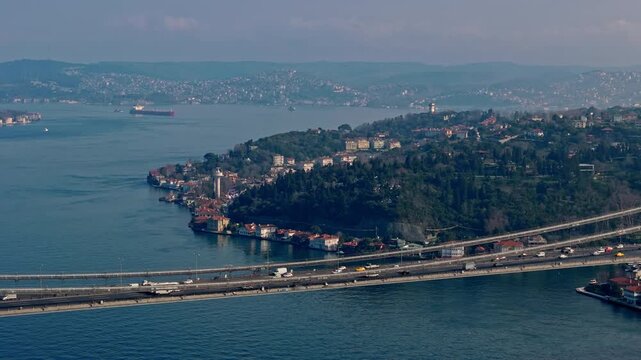Aerial drone footage of the Istanbul Bosphorus, featuring the 15 July Martyrs Bridge, coastal neighborhoods, red-roof houses and wide blue waters, presenting a clear panoramic view of the city.