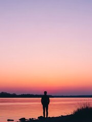 Silhouette of a person standing by a serene lake at sunset