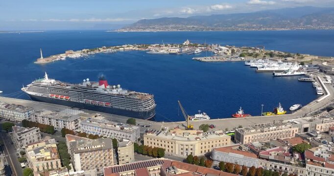 Aerial view of the city port of Messina, Sicily, Italy. Panorama of a crescent-shaped natural harbor. A large cruise ship and various vessels are docked along the quay.The city center is in foreground